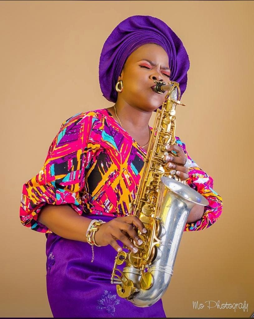 Funmisax seated with saxophone and hat